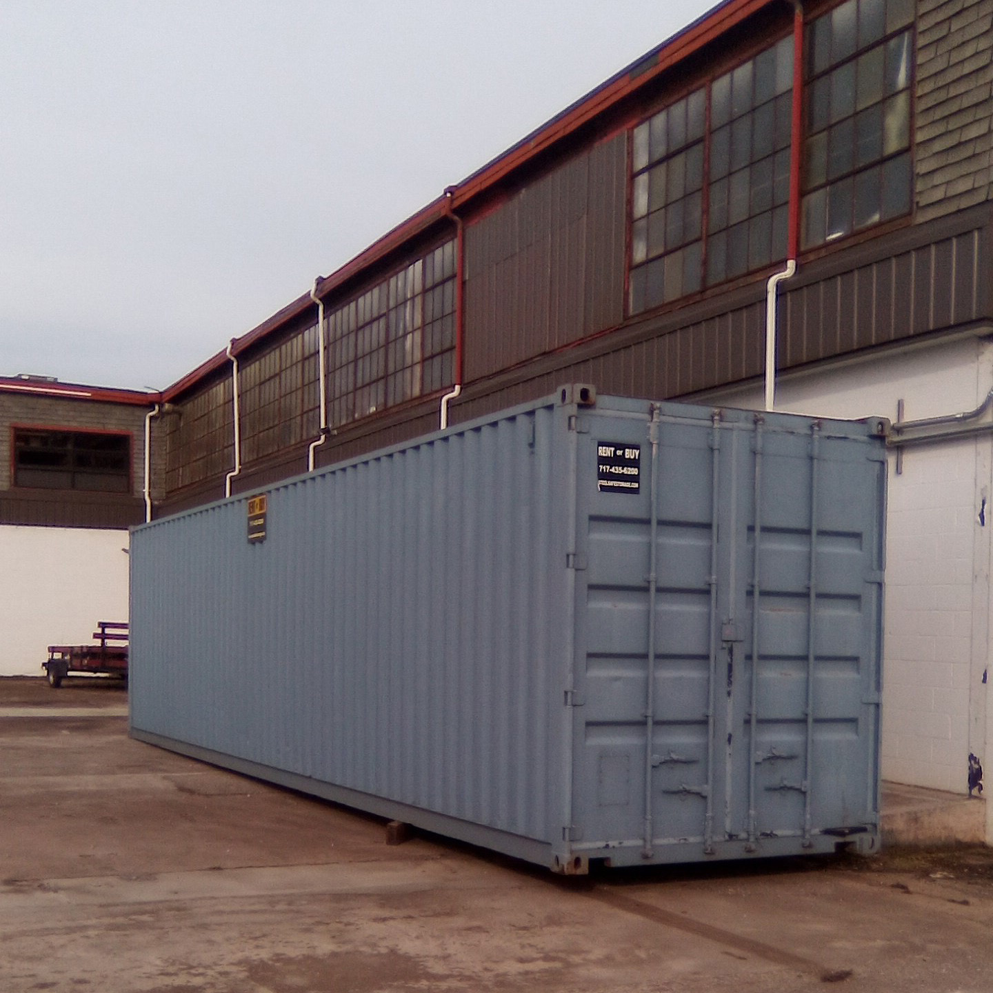 Portable Container Storage Industrial A large light blue shipping container is placed on a concrete surface beside an industrial building with large windows.