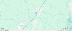 Map view showing a town intersected by major roads and surrounded by green areas, with blue lines indicating waterways and a highlighted central location.