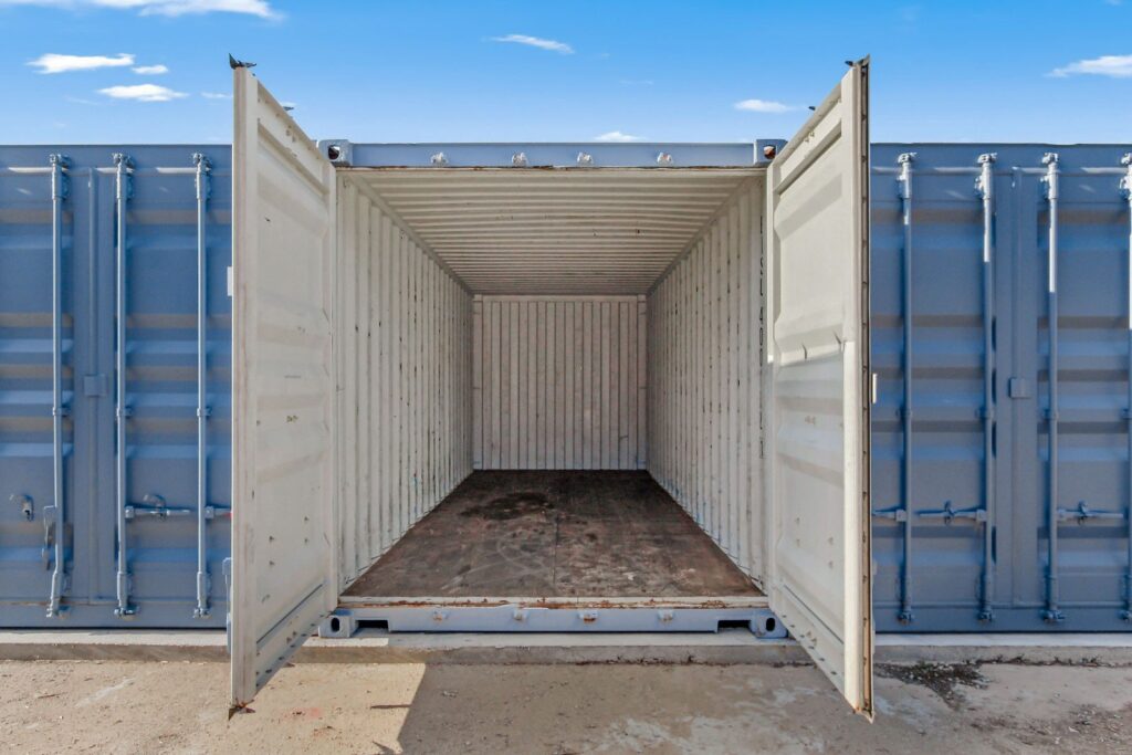 Open doors of an empty blue shipping container, showing its interior with a metal floor and walls, under a clear sky.